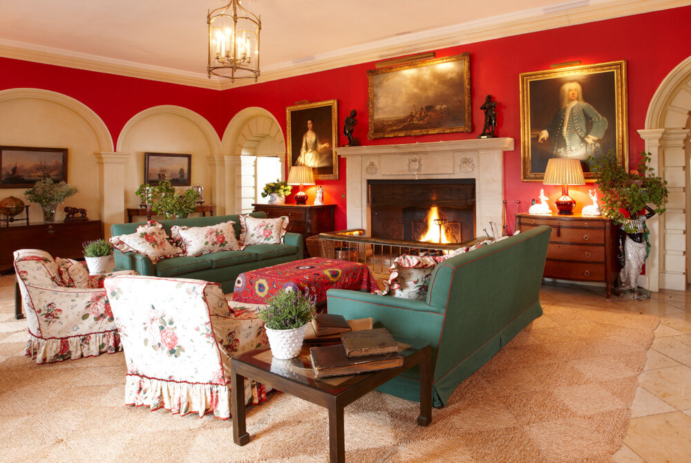 Rich red room with large stone white fireplace and green armchairs