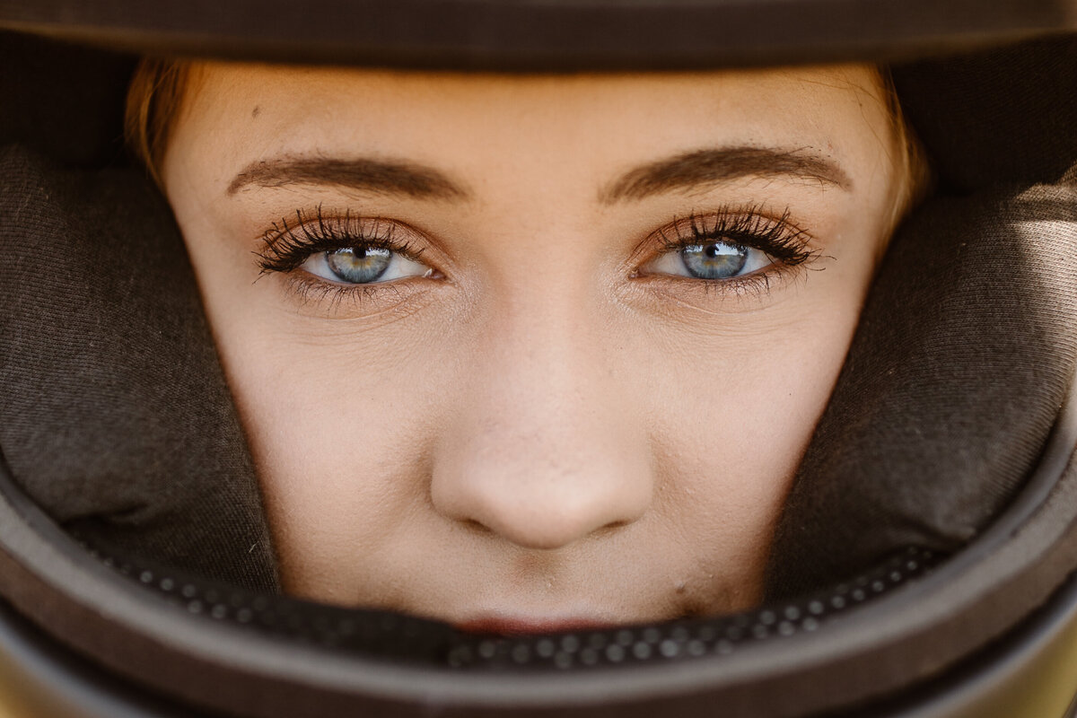 Close-up portrait of a woman with striking blue eyes, framed by the padding of a helmet, capturing emotion and detail.
