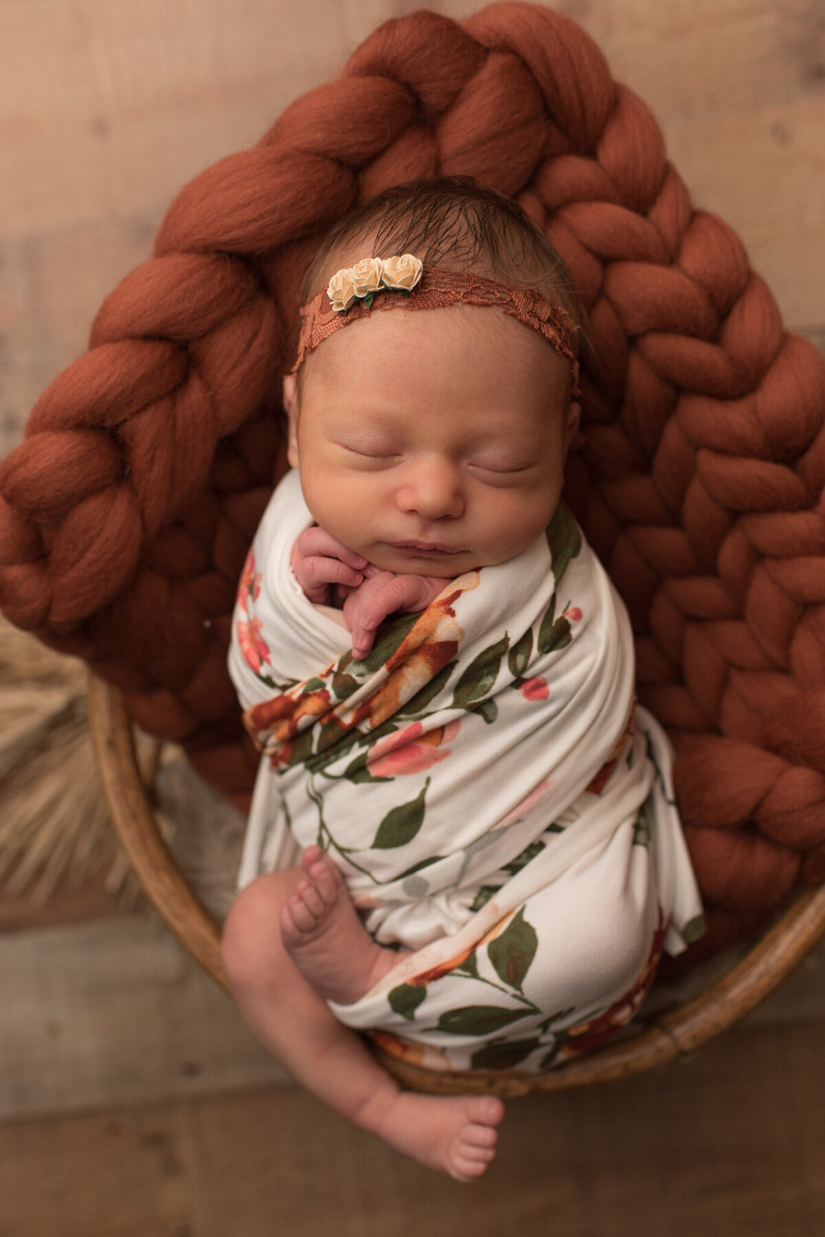 Baby girl is wrapped in fall-themed floral wrap with burnt orange headband in basket