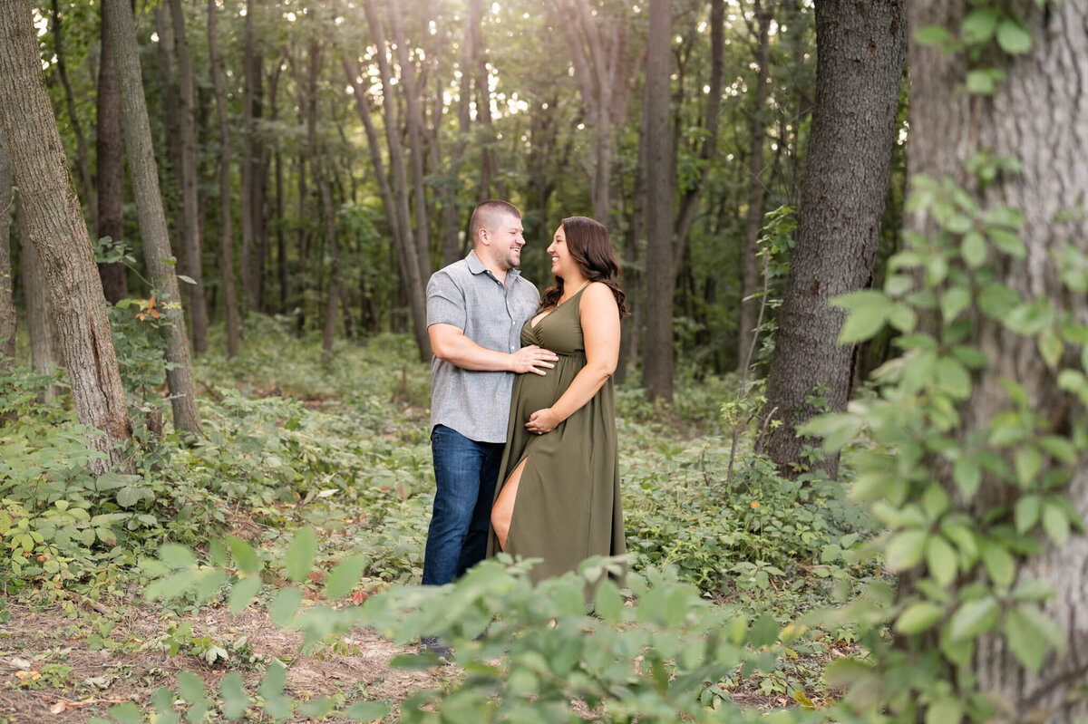 maternity couple standing in a beautiful forest looking happy