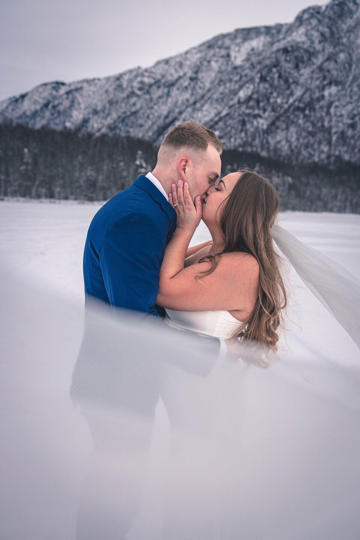 An Alaska military couple kisses while her veil catches the wind