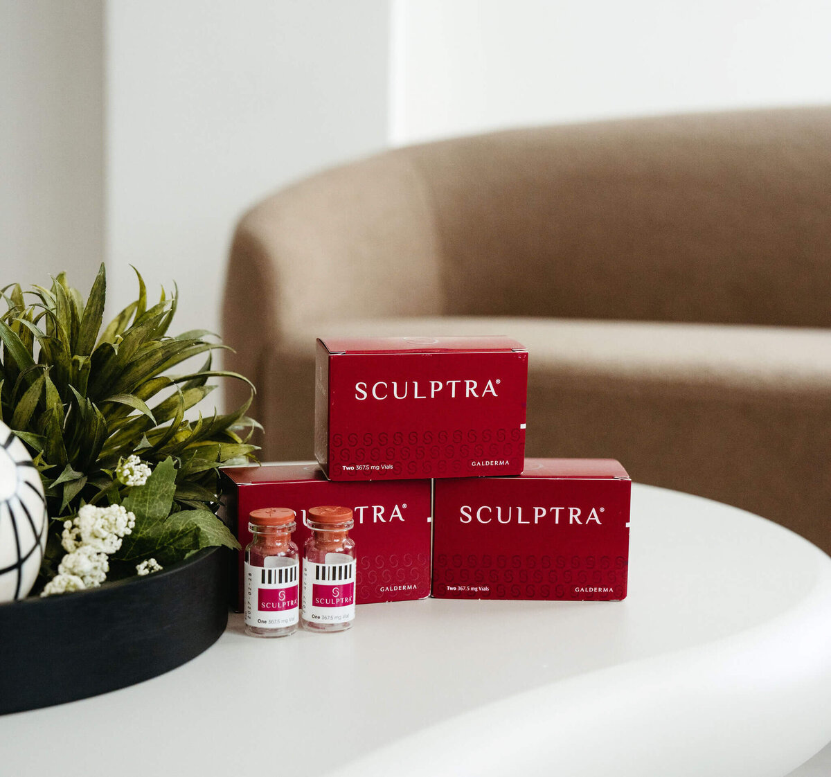 Sculptra vials and packaging arranged on table beside floral centerpiece at Maxwell Aesthetics Salem studio