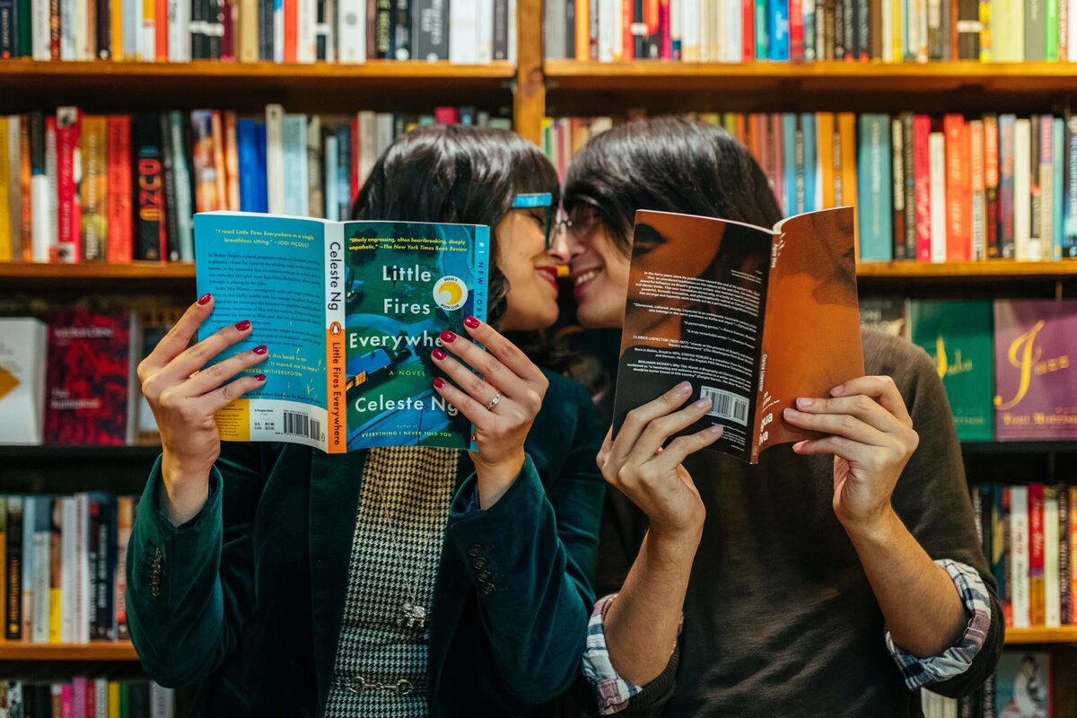 A couple about to kiss as they hold up books.