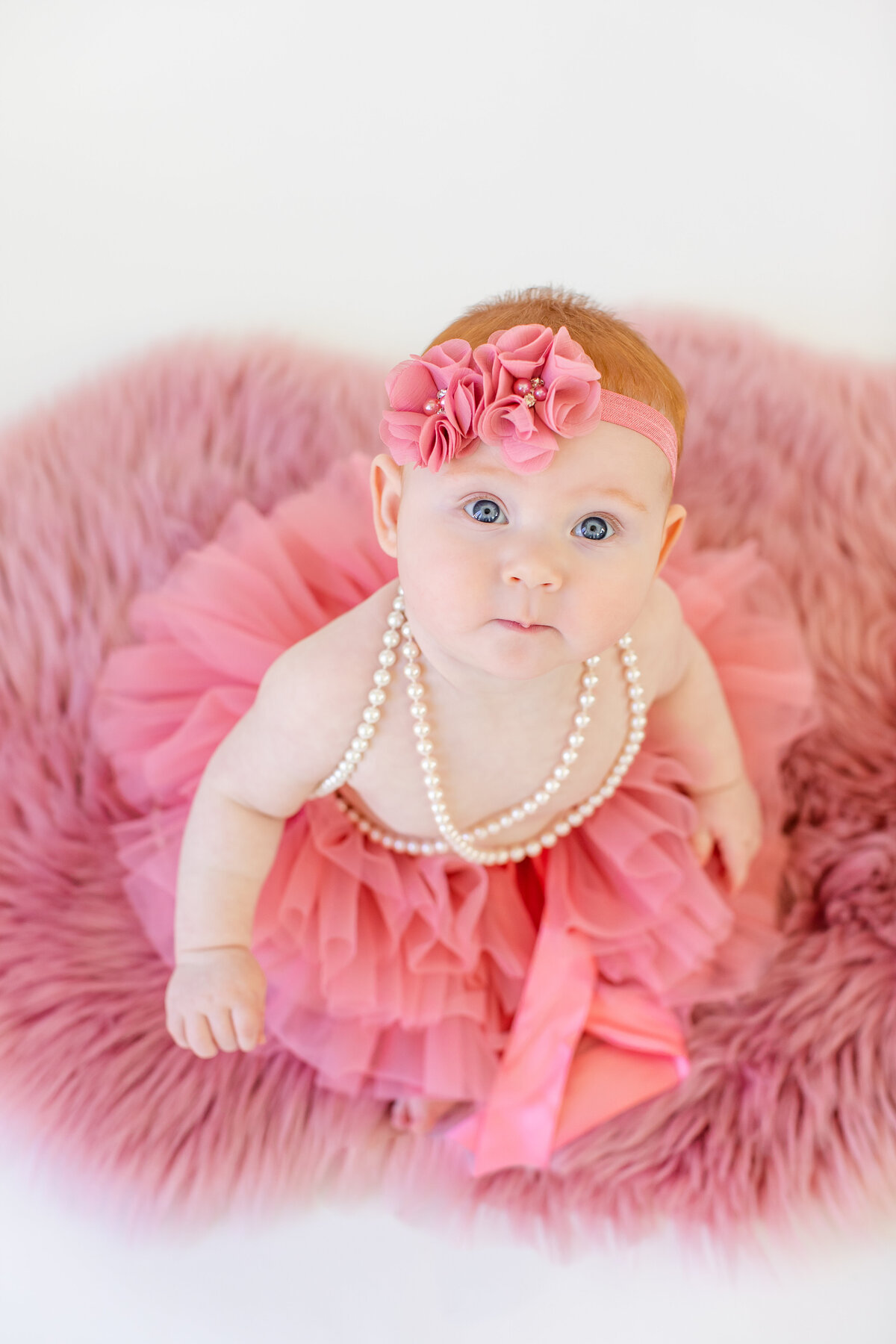Baby girl in pink tutu and pearls looking up at camera