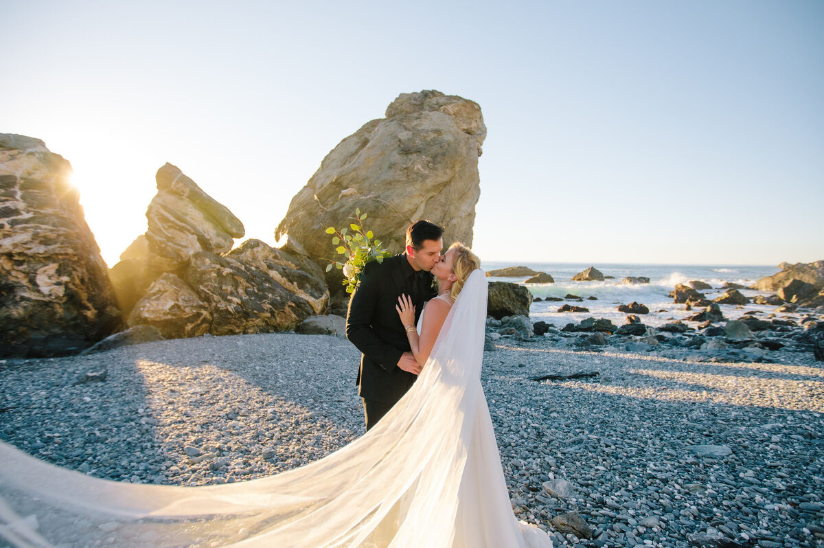 bride and groom kiss on rock beach