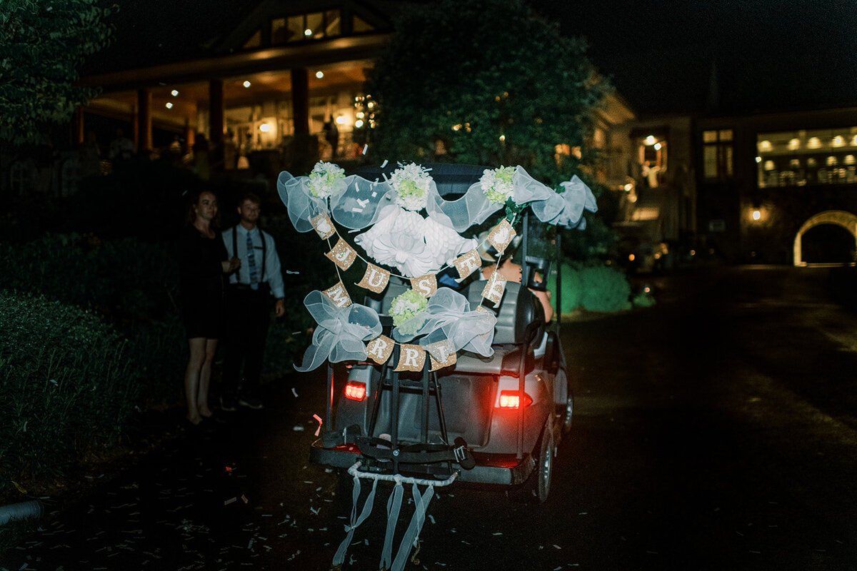 Decorated golf cart with “Just Married” sign as the couple leaves their mountain wedding reception at night.