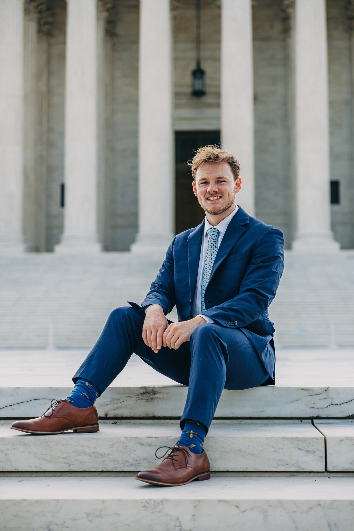 A newly graduated young man who is sitting in front of SCOTUS wearing a suit
