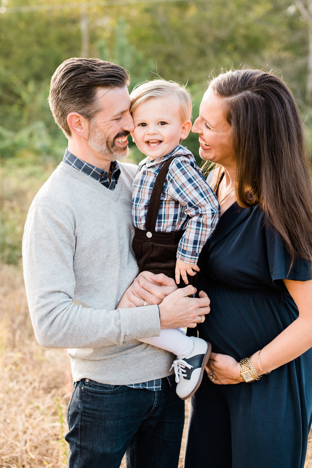 Pregnant mom and her husband hold their toddler and laugh during a Raleigh maternity photo session. Photographed by Raleigh NC Family Photographer A.J. Dunlap Photography.