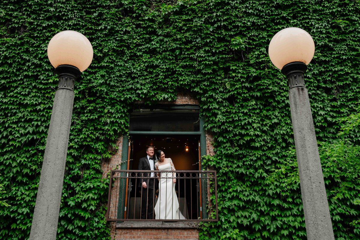 Bride and groom look out window surrounded by Ivy