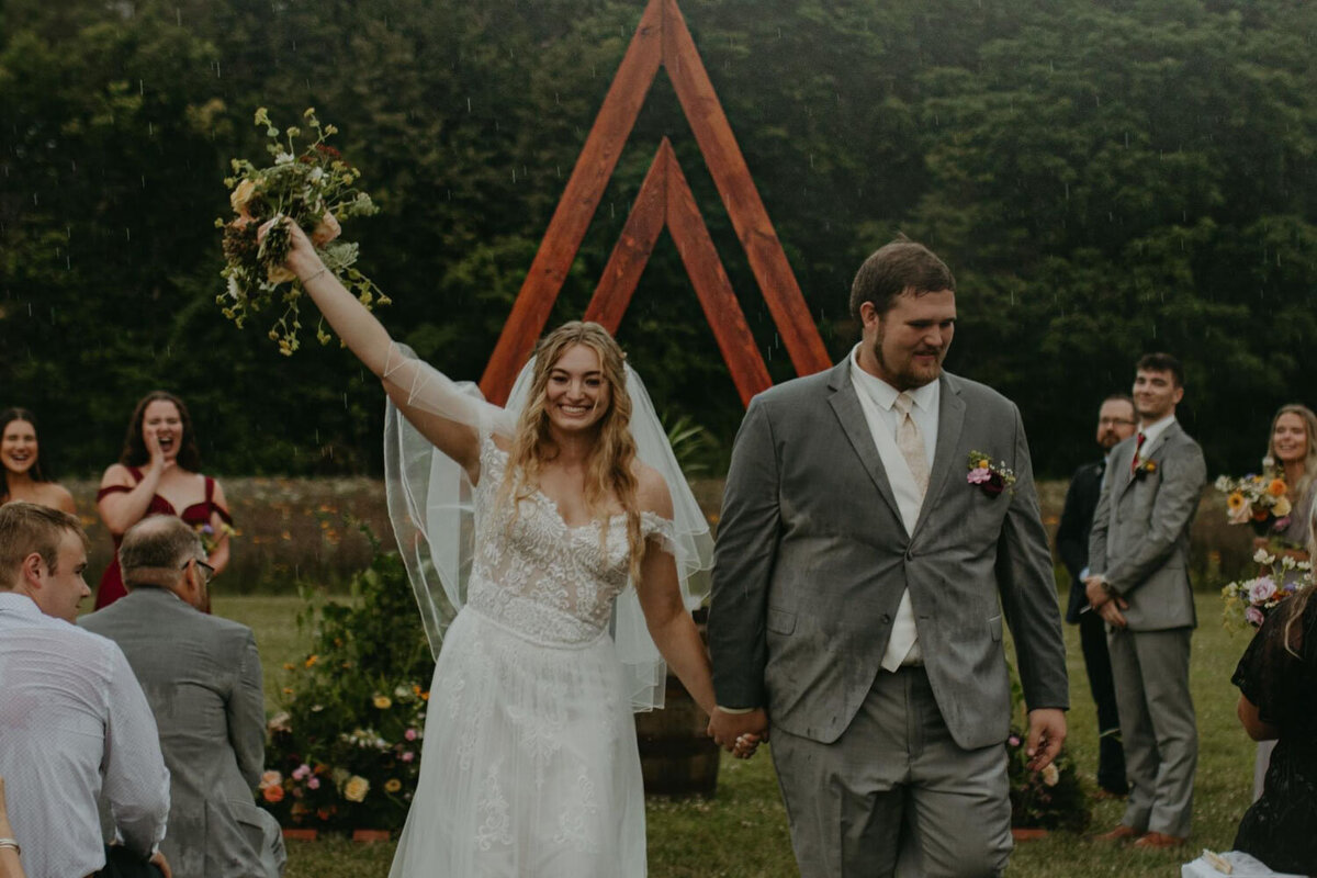 Bride and groom walking down the aisle, bride raising bouquet in celebration