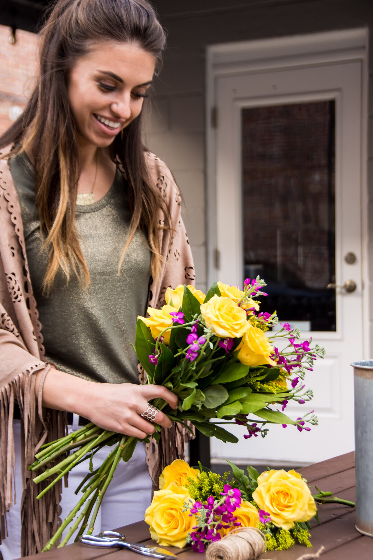 Smiling florist looks down at a bouquet of yellow and purple flowers