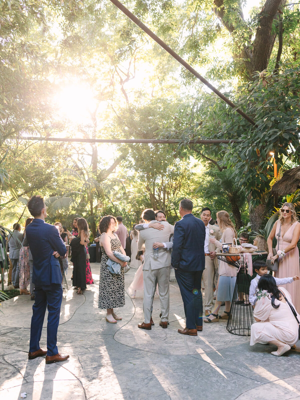 A lively outdoor gathering in a lush setting, with friends mingling and celebrating, illuminated by warm sunlight.