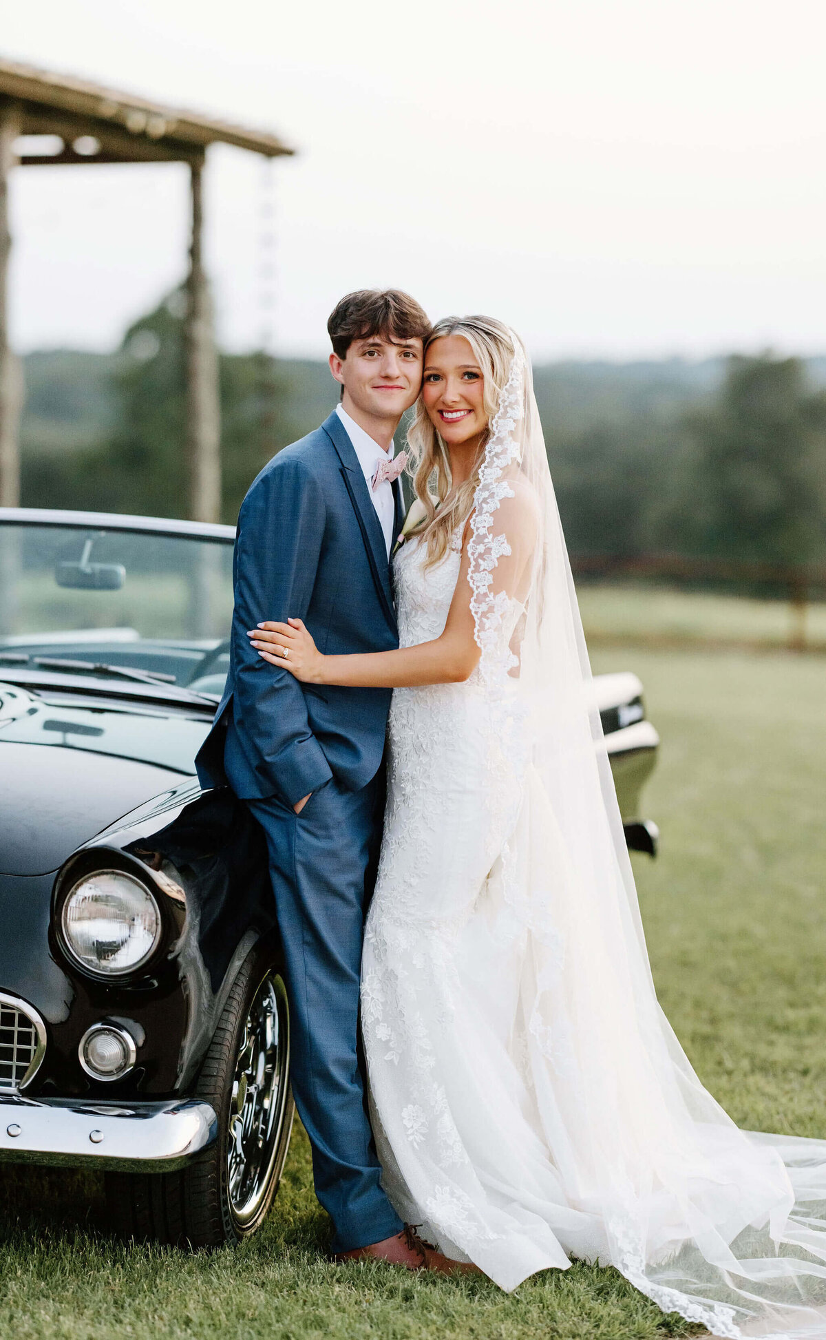 bride and groom leaning against vintage black car for wedding day portraits at East Texas wedding venue after wedding ceremony