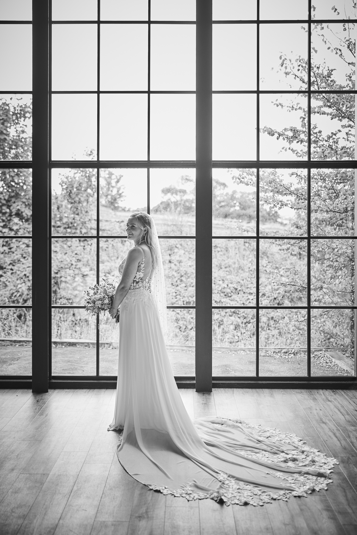 Bride stood holding flowers in the grand window of wedding venue
