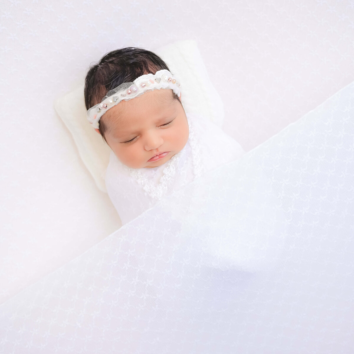 Newborn swaddled and tucked in with a sheer white blanket for a newborn photo session.