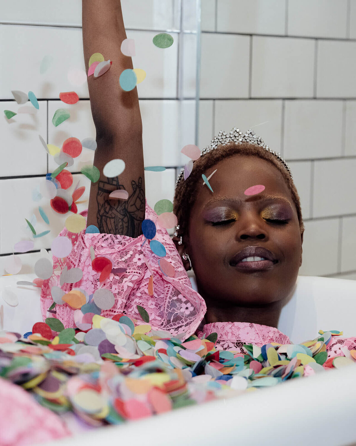 A bride in a pink dress and crown bathes in a bath of colourful confetti.