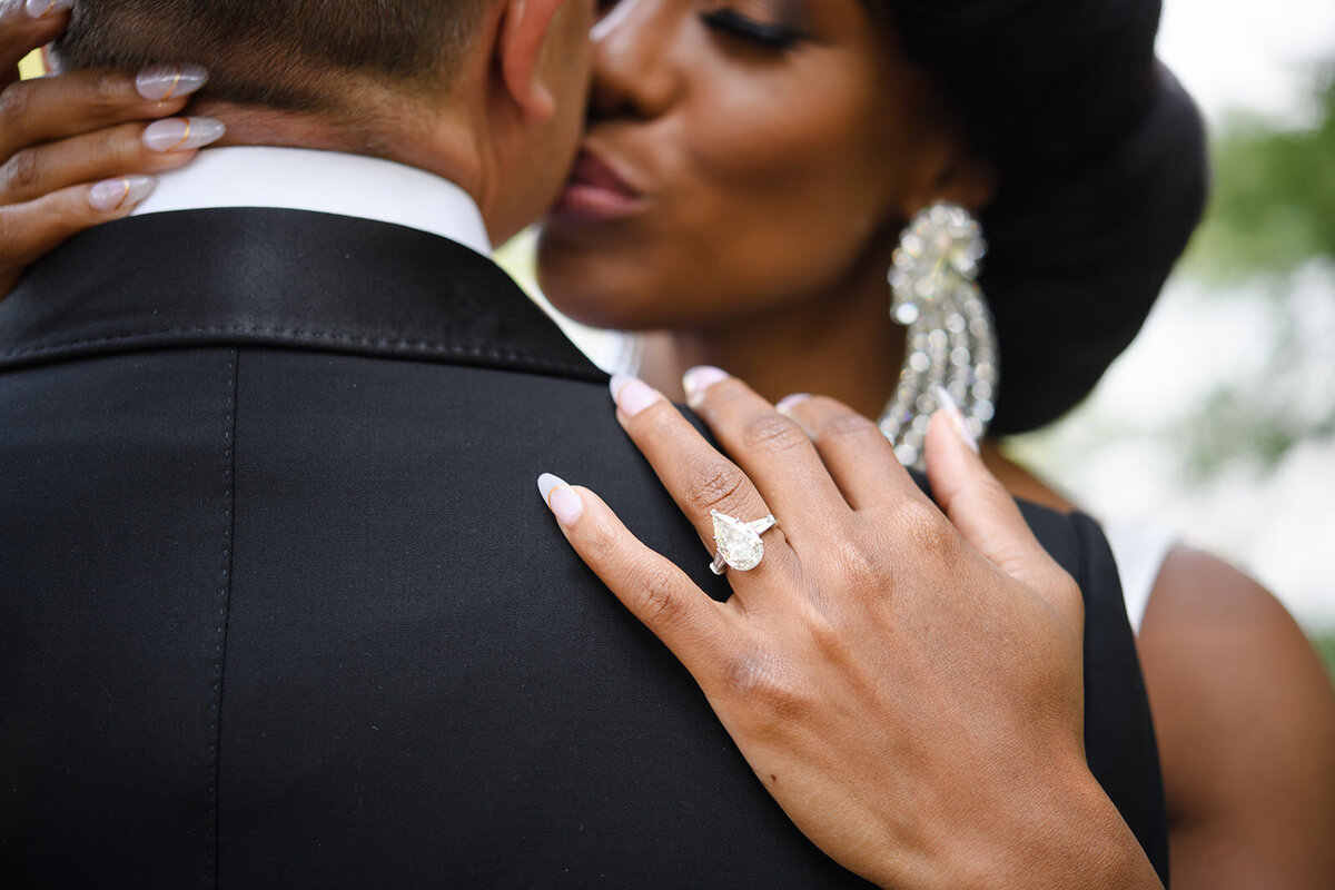 Intimate moment captured as the bride kisses the groom, showcasing her sparkling ring.