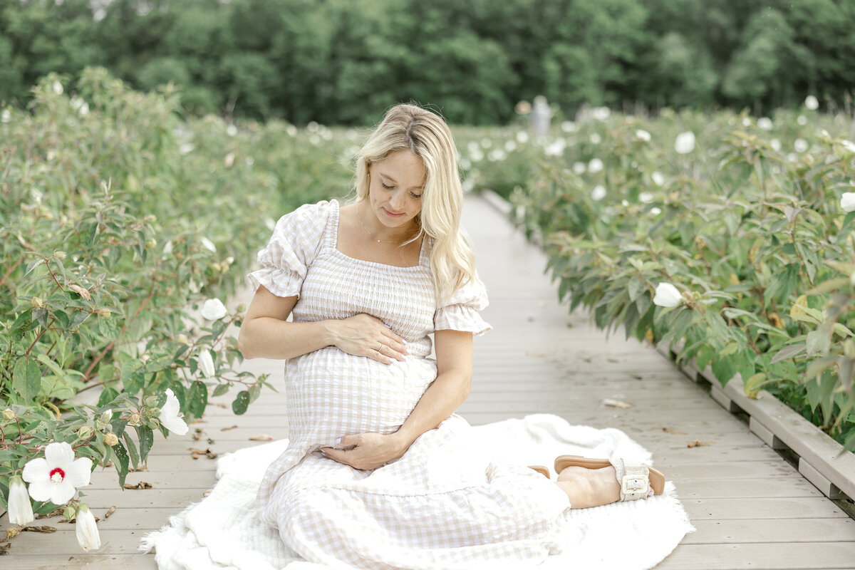 Pregnant woman sitting on a boardwalk in Alexandria, Virginia surrounded by flowers