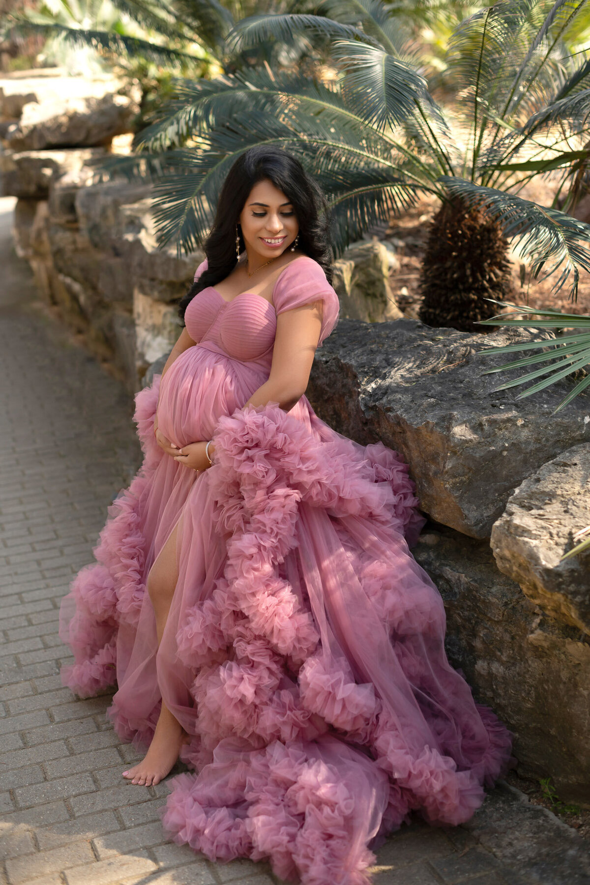 Dramatic maternity portrait in voluminous pink gown against desert landscape backdrop