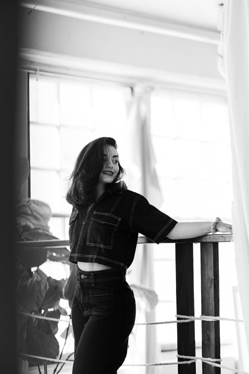 Portrait d'une femme en noir et blanc, tenue en jean, bras reposant sur une rembarde en bois, lors d'un shooting photo.