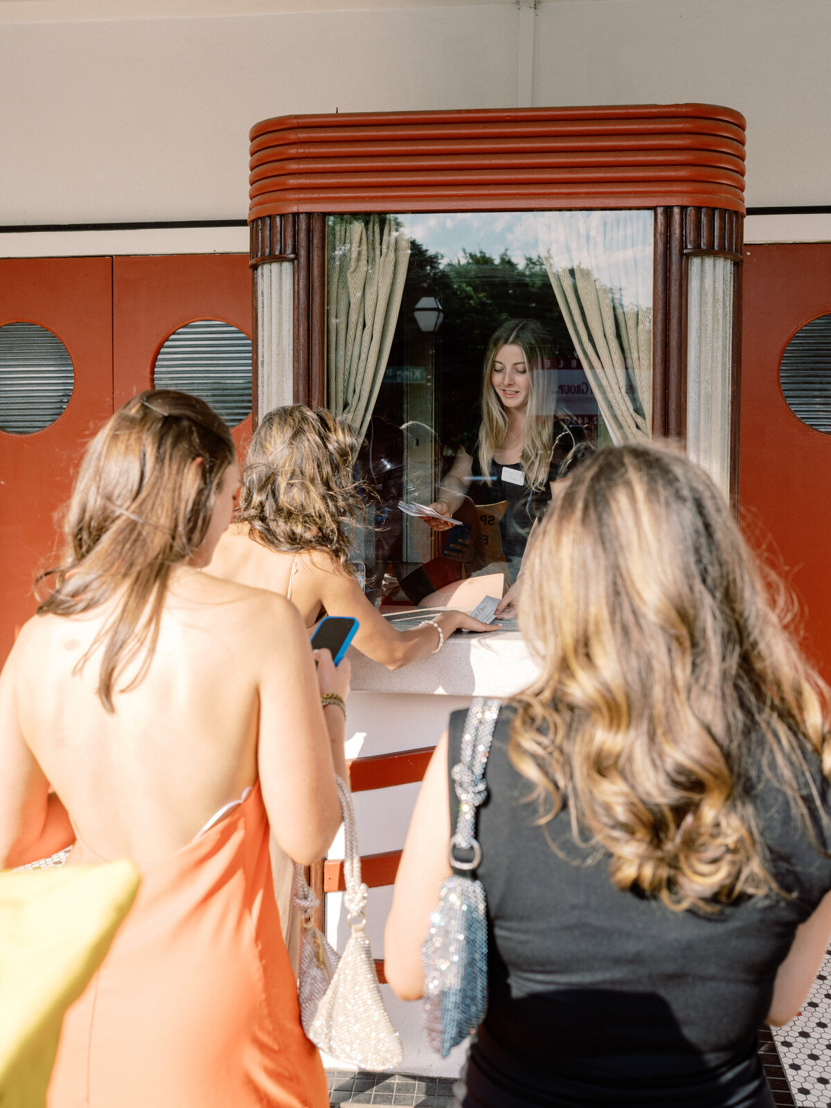 Guests line up at a charming vintage check-in booth, eagerly arriving at a joyful wedding ceremony while dressed in fashionable attire.