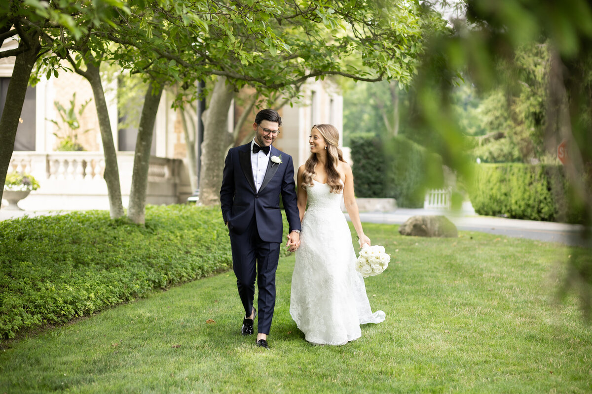 A bride and groom walk hand in hand outside sleepy hollow country club on the day of their wedding