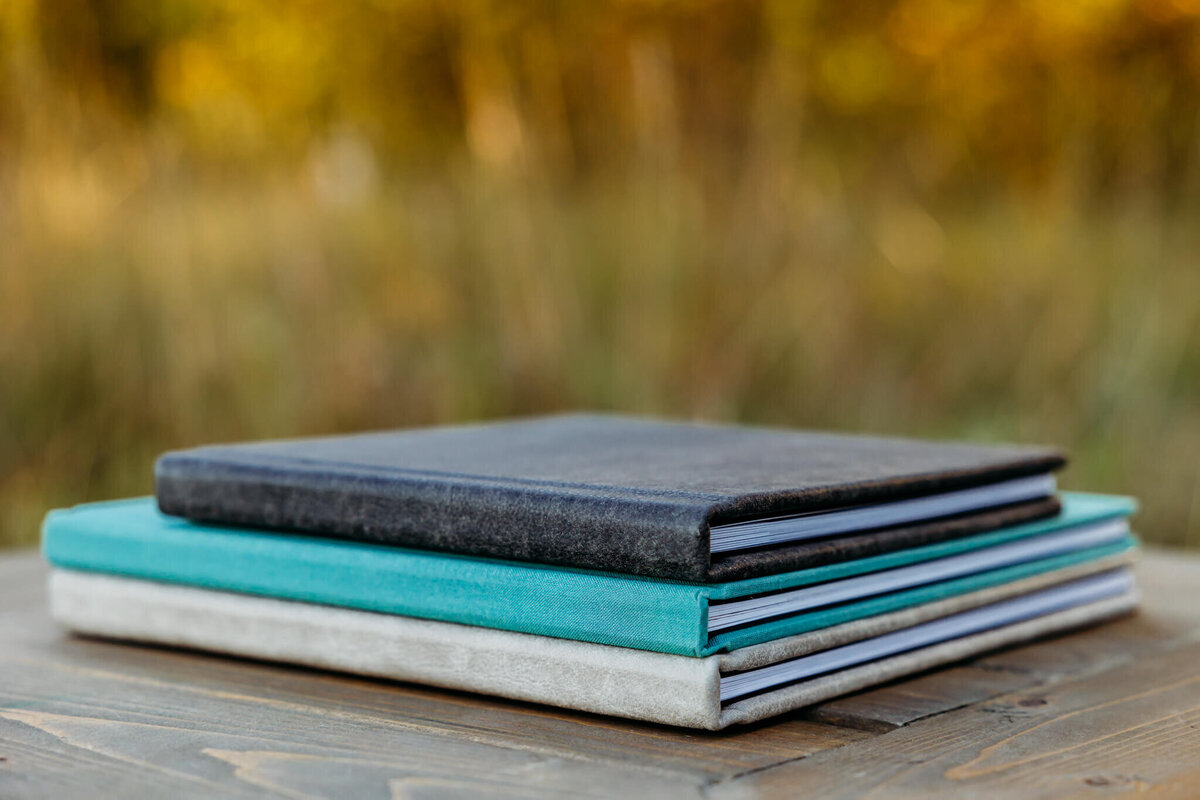 a grey, teal and black album stacked on top of each other on a wooden table in a grassy field