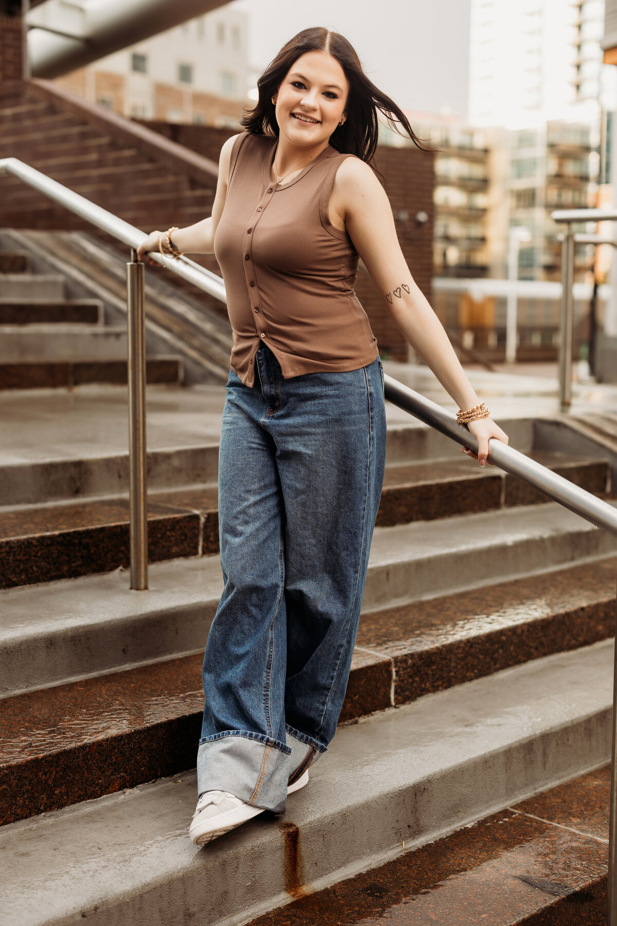 high school senior girl stands with her back against a metal stair rail in downtown Denver for her urban senior photos