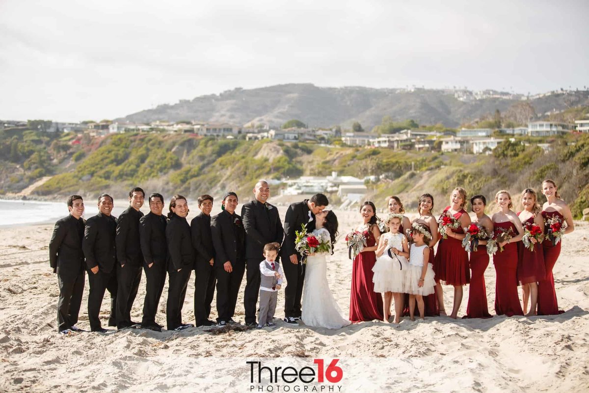 Bridal Party is all smiles as the Bride and Groom share a kiss on the beach