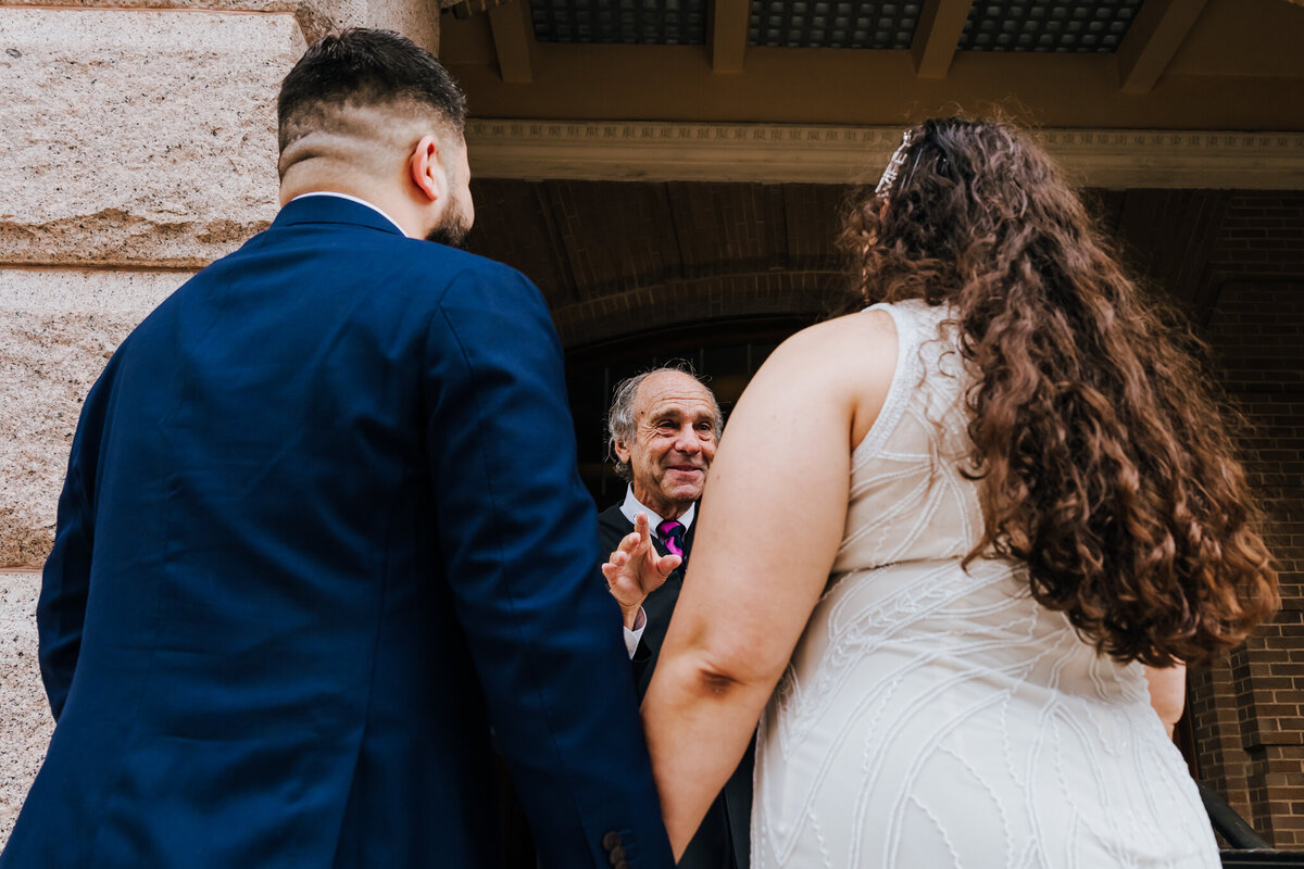 Bride and groom standing outdoors during their courthouse wedding ceremony in Houston, TX. An older man, possibly the officiant or a family member, smiles warmly in the background. Captured by ShutterUp Photography.