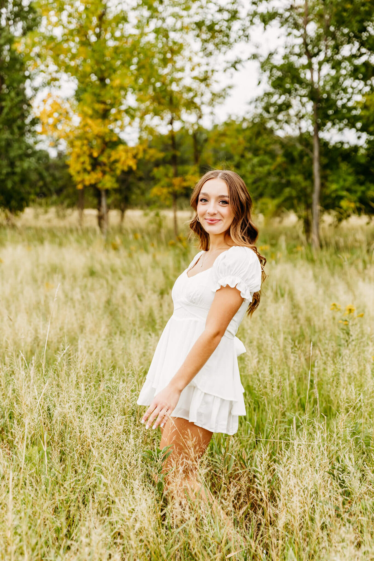 super pretty teenage girl in a short white dress playing with the grasses as she walks through a field.