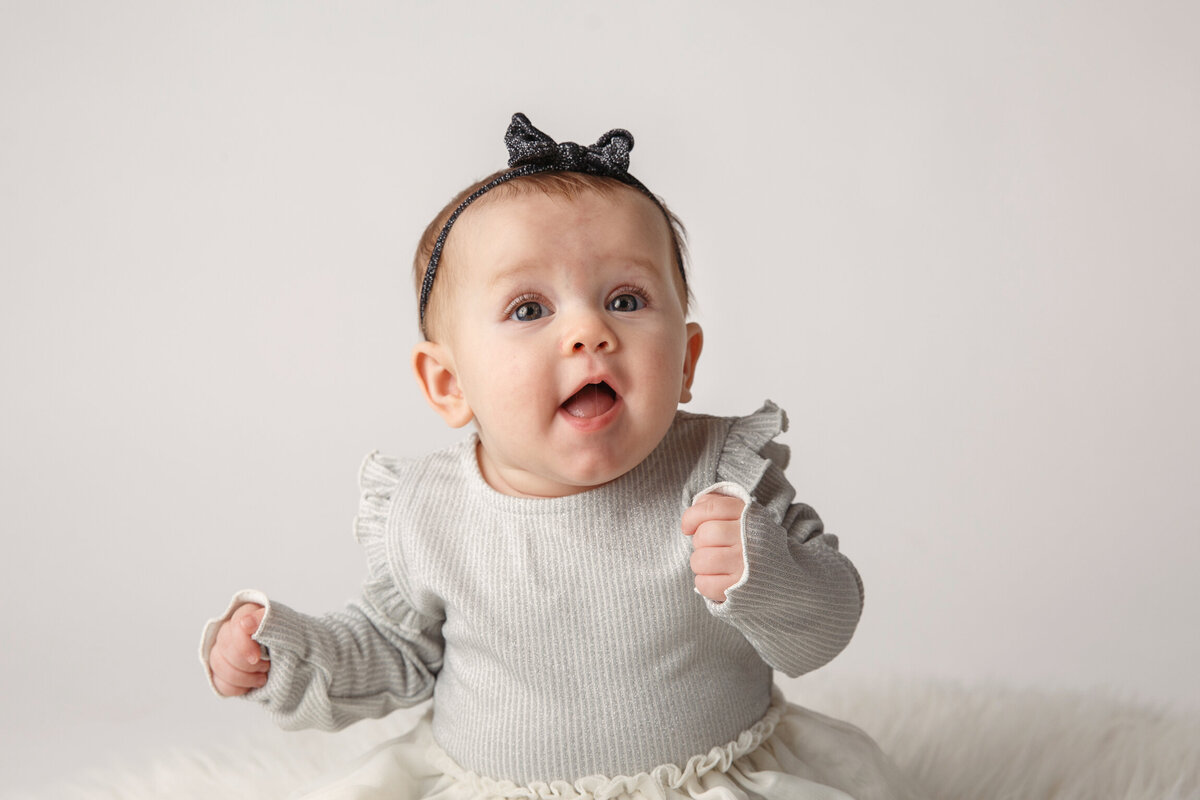 Cute six month old baby wearing a white dress and phtographed on a white background