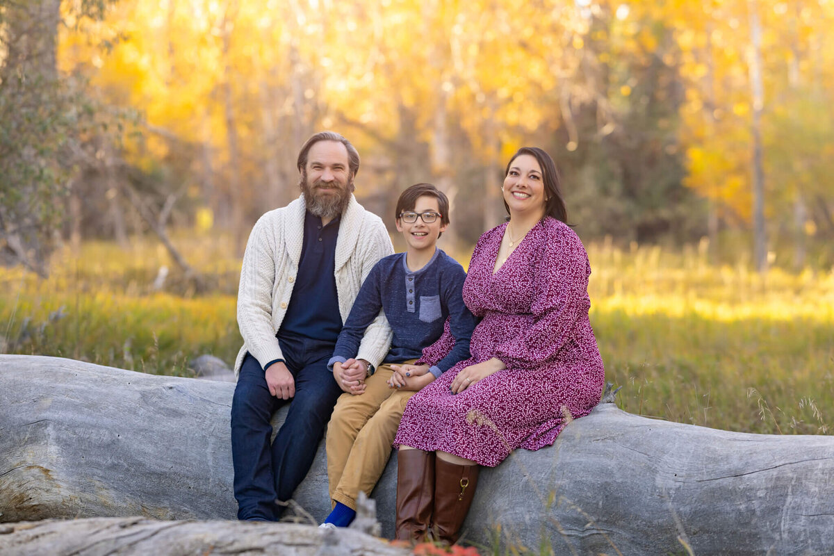 family of three sitting on a log in a forest