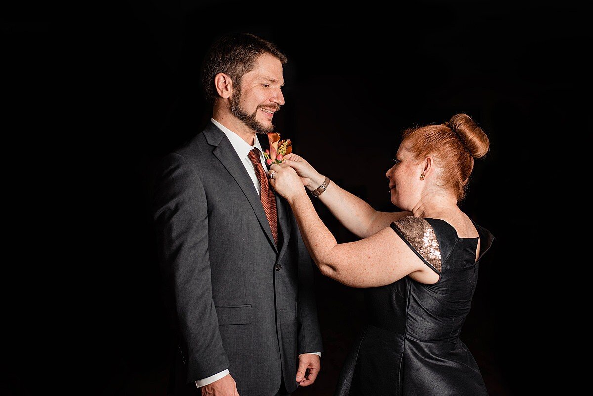 Wedding planner with Weddings & Events by Raina pins the boutonniere onto the groom