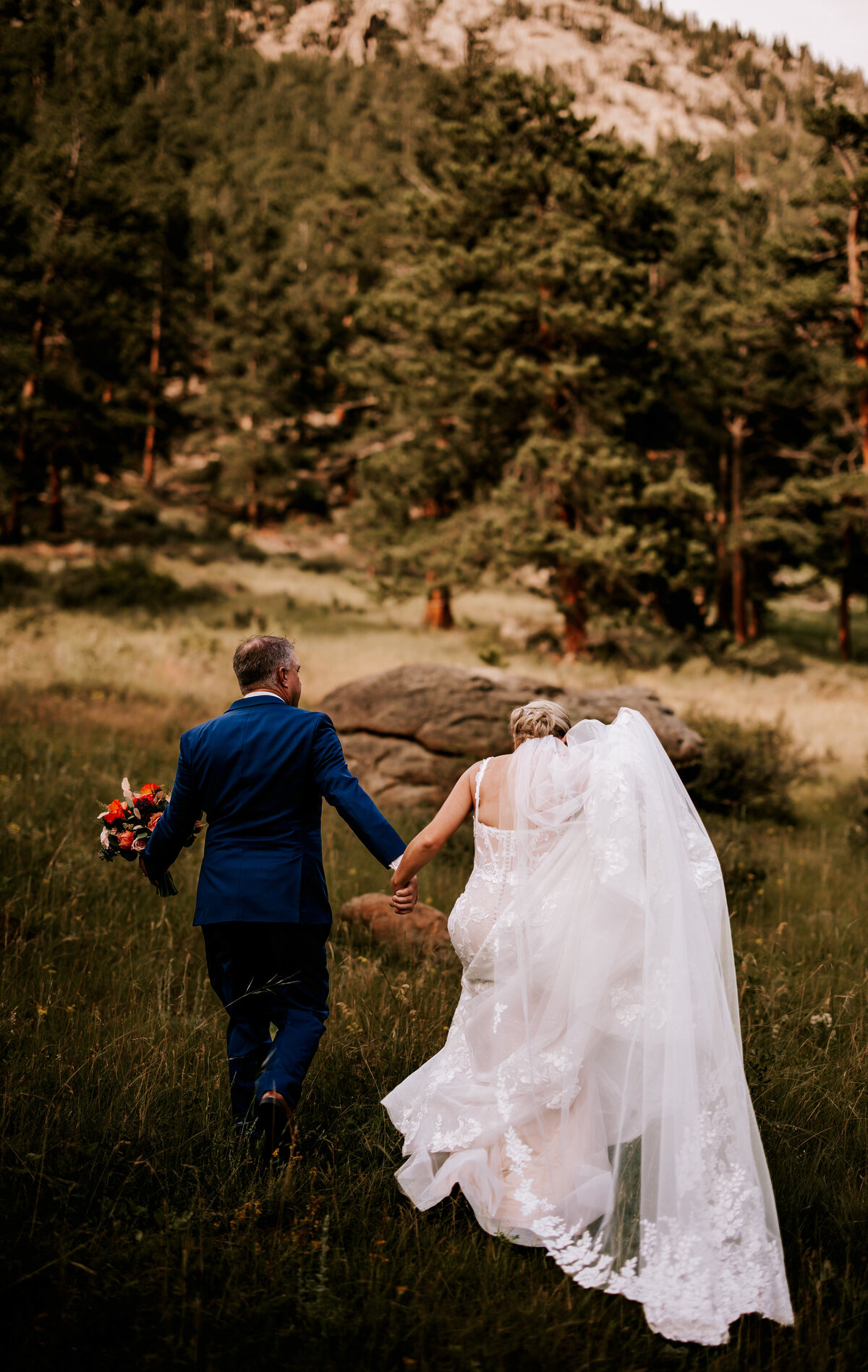 Bride and groom leading each other through a tall field of grass in Rocky Mountain National Park