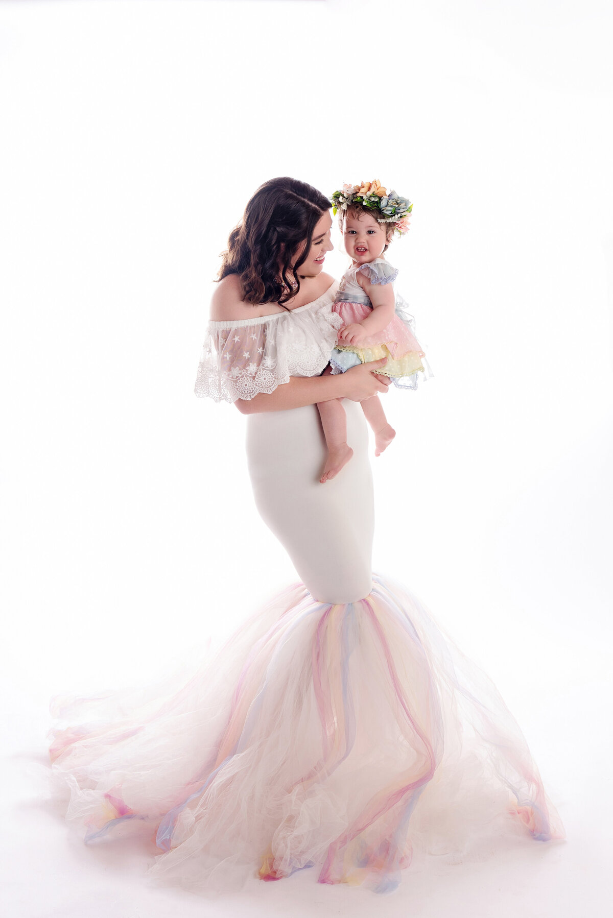 st-louis-family-photographer-mom-in-pastel-rainbow-mermaid-fit-dress-holding-baby-girl-on-whtie-backdrop