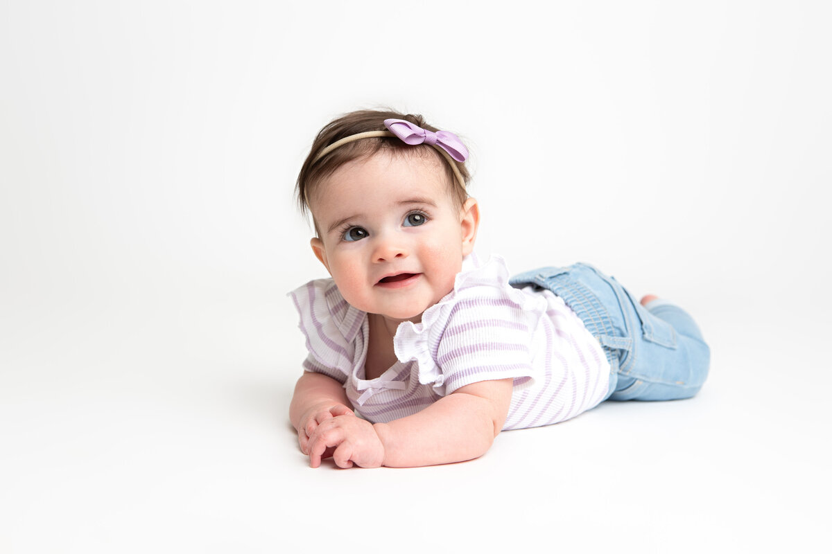 6 month old girl laying on a white backdrop