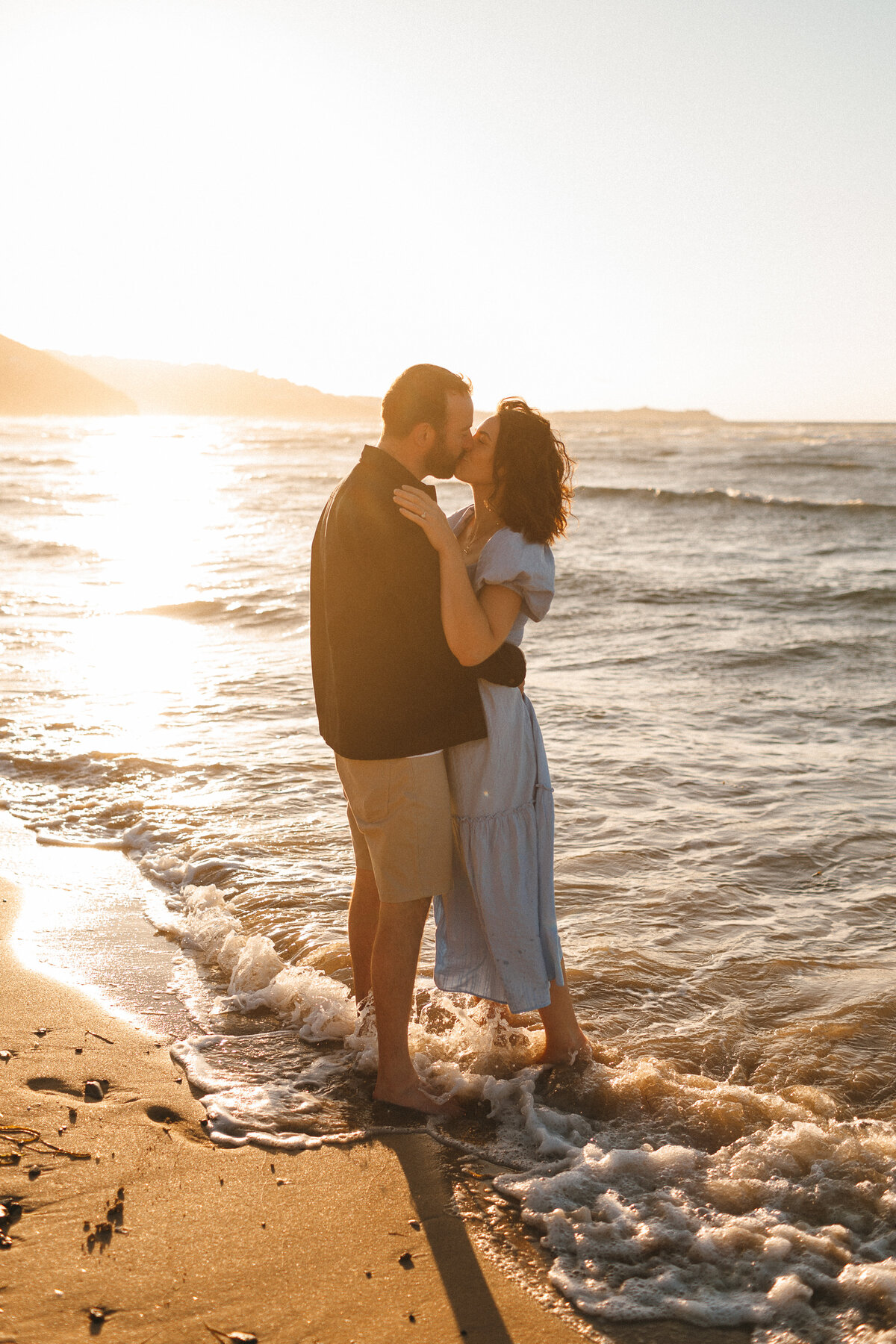 Photograph of a young  engaged couple at the beach in West Cornwall on a sunny day standing in the sea