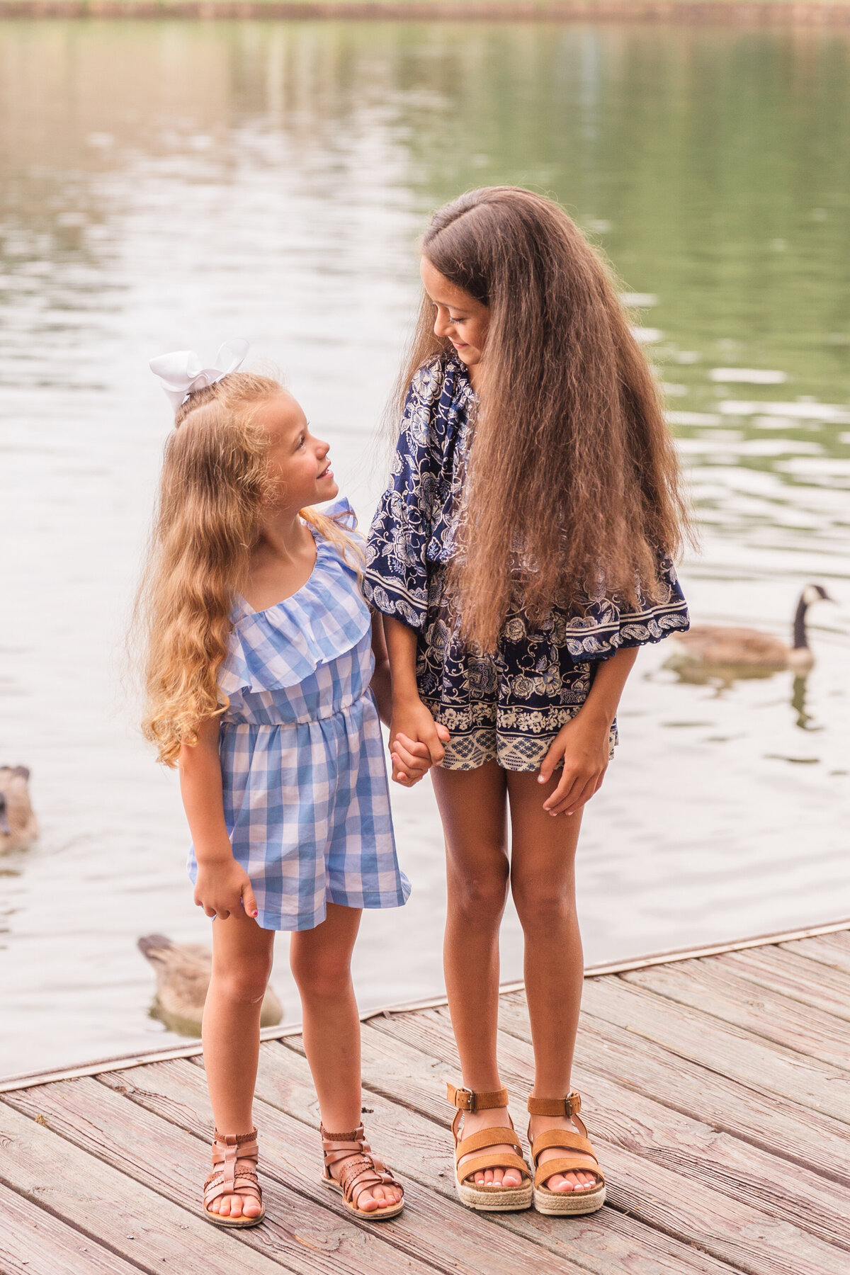 sisters hold hands on a lake dock