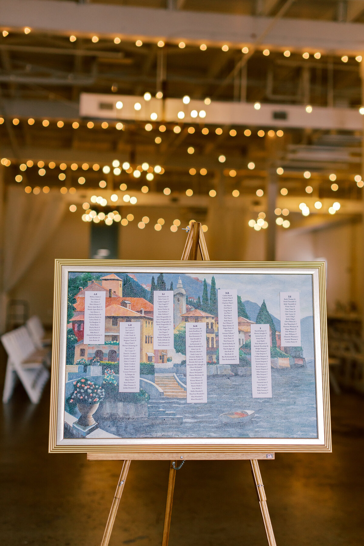 Artistic seating chart on easel surrounded by twinkle lights at Brendan and Sara’s Fetewell wedding reception.