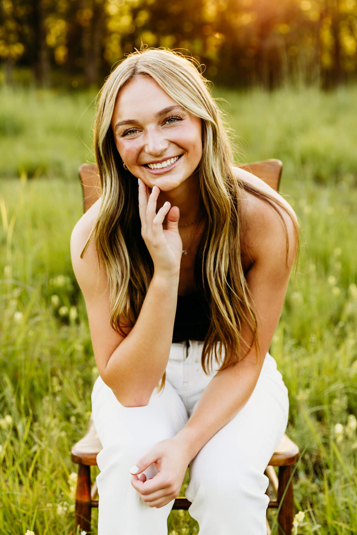 photo of a beautiful teenage girl sitting on a wooden  chair and learning forward on her knees captured by Ashley Kalbus Photography