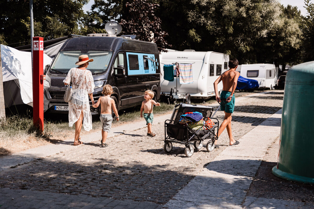 moeder loopt met zoons over campingpad oudste jongen trekt de bolderkar met spullen