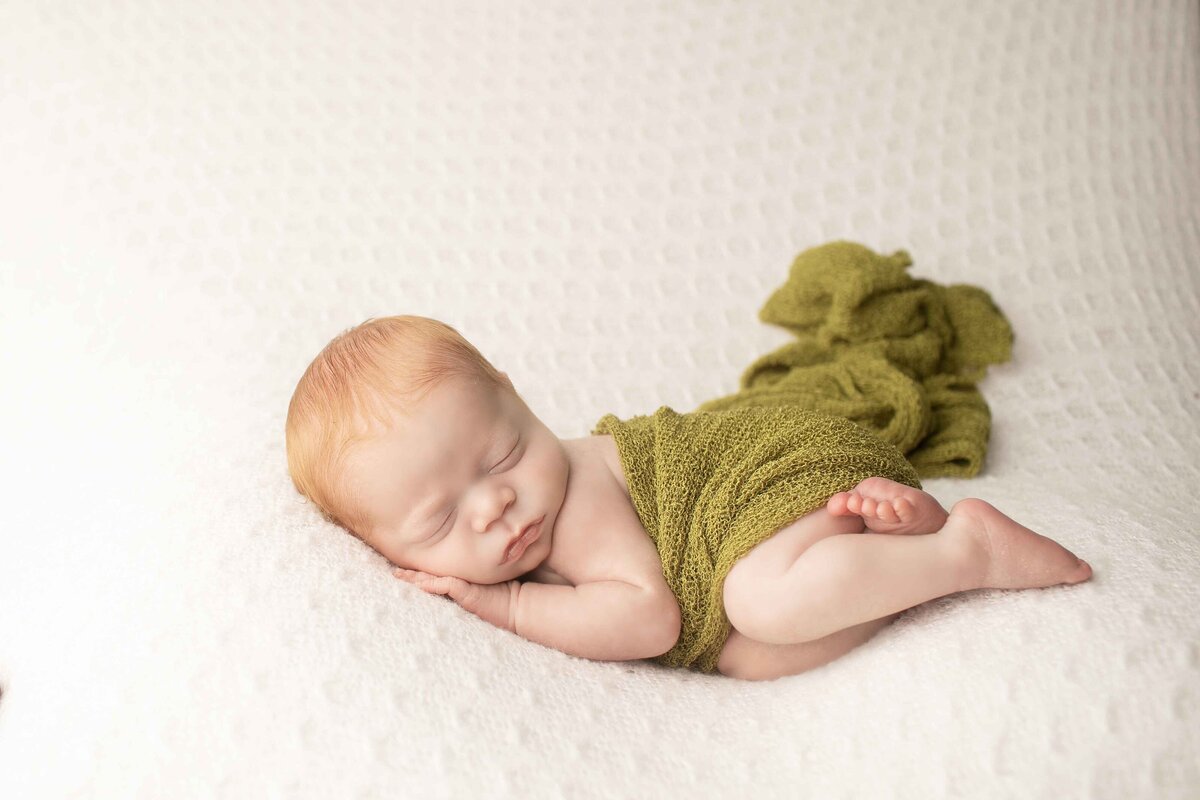 Sweet red-headed newborn boy wrapped and posed on a plush backdrop, capturing his delicate and peaceful expression