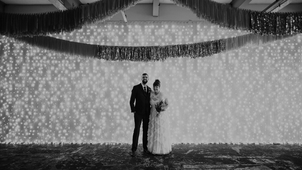Bride and groom stand in front of a wall of lights at Trafalgar Warehouse in Sheffield.
