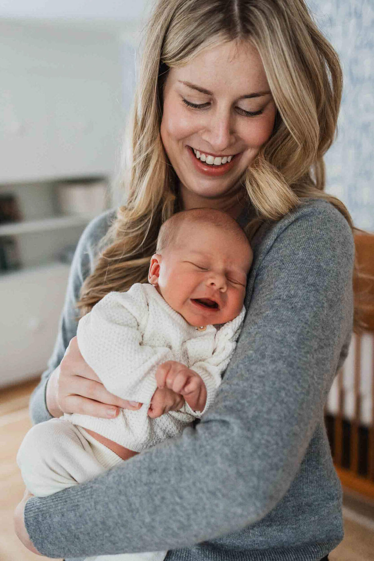 A happy mother holds her newborn close in nursery during a Cleveland newborn photography session.