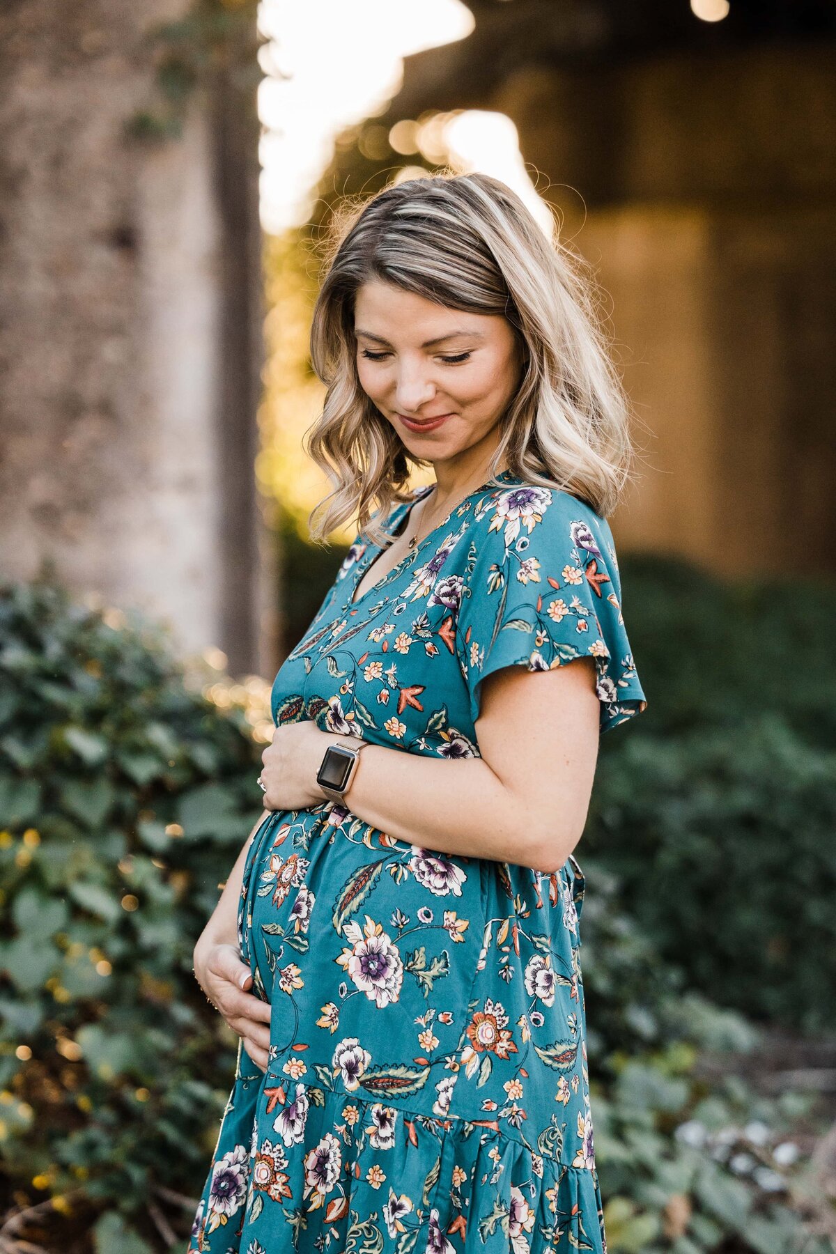 Pregnant woman smiling and touching her belly outdoors during her maternity photography session.