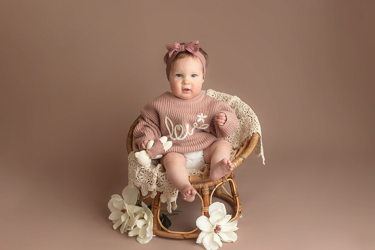 One year old little girl in a papasan chair on mauve backdrop.