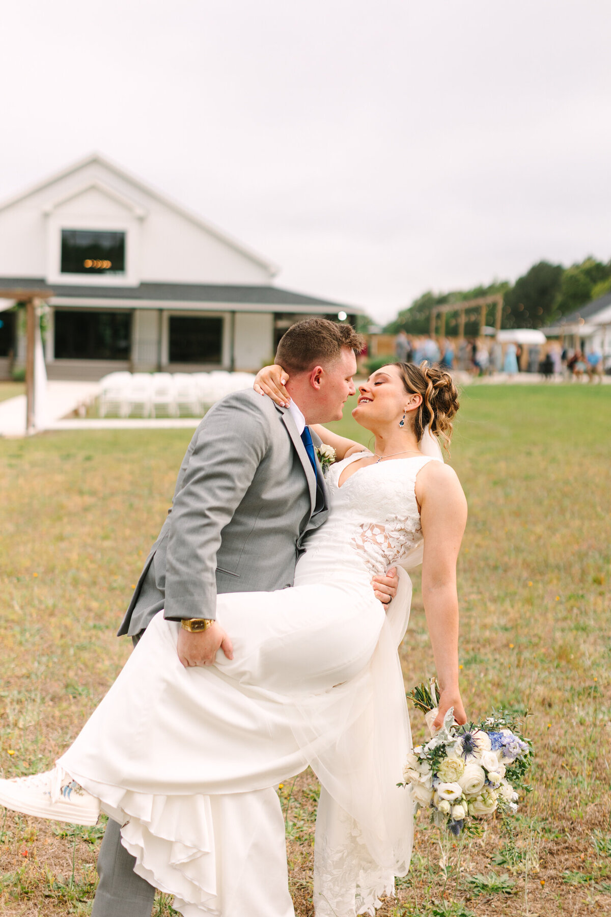 Candid moment of bride and groom dip and kiss behind the ceremony space at New Branch Farms