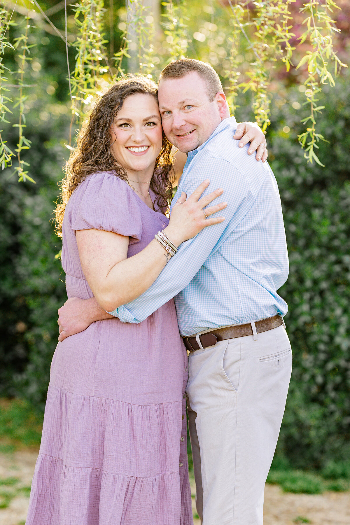 Couple stands with sunlit willow tree at 9 Oak Farms for engagement session, Monroe, GA. 