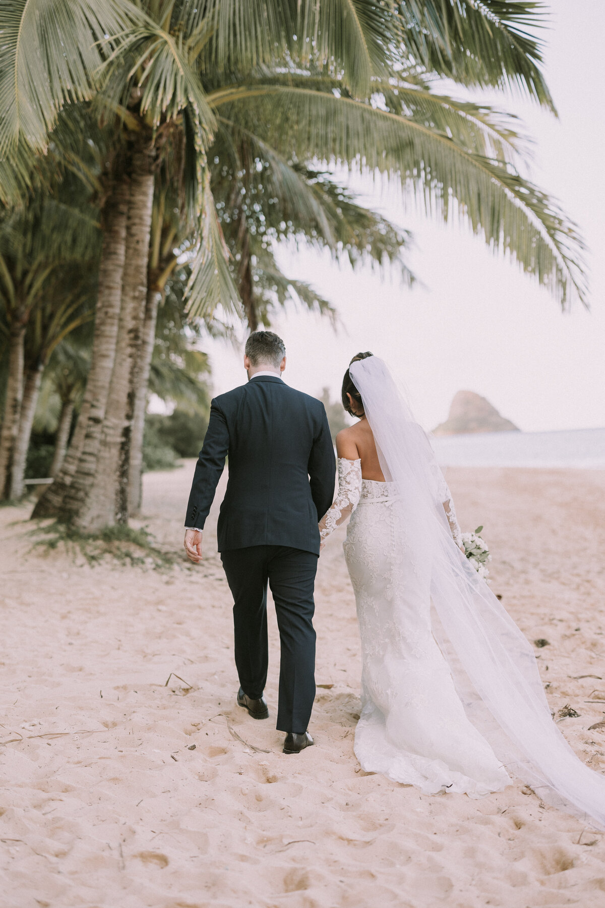 Bride and groom walking downt he beach towards palm trees and china mans hat